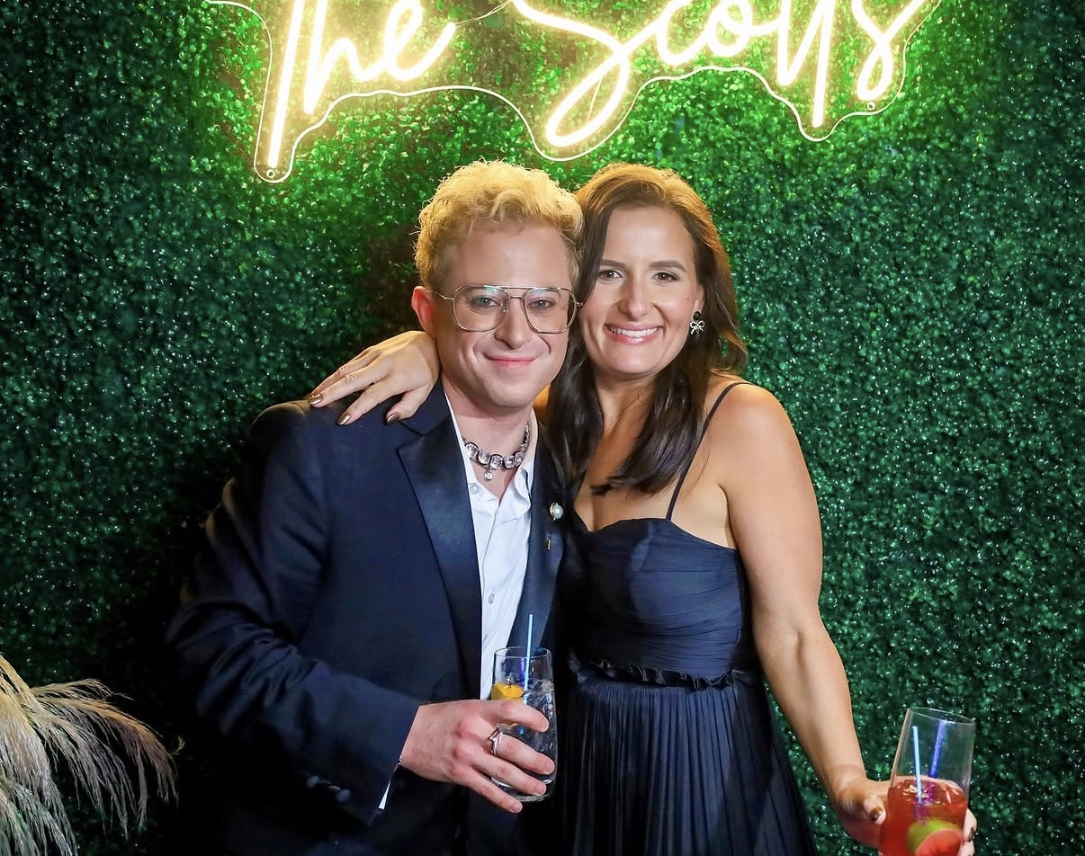 Couple posing at greenery wall with neon sign photo booth