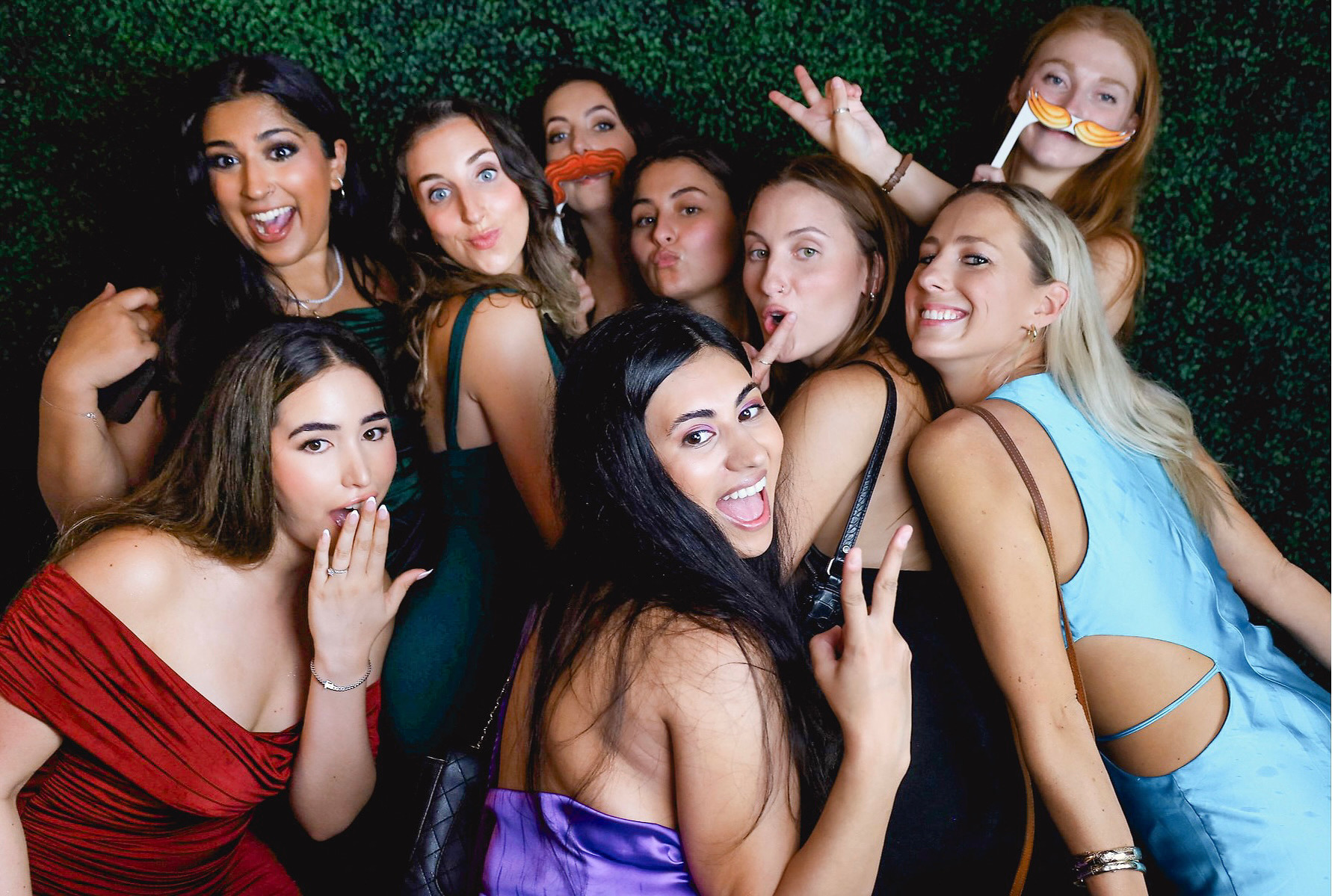 Group of friends with props at photo booth with greenery backdrop