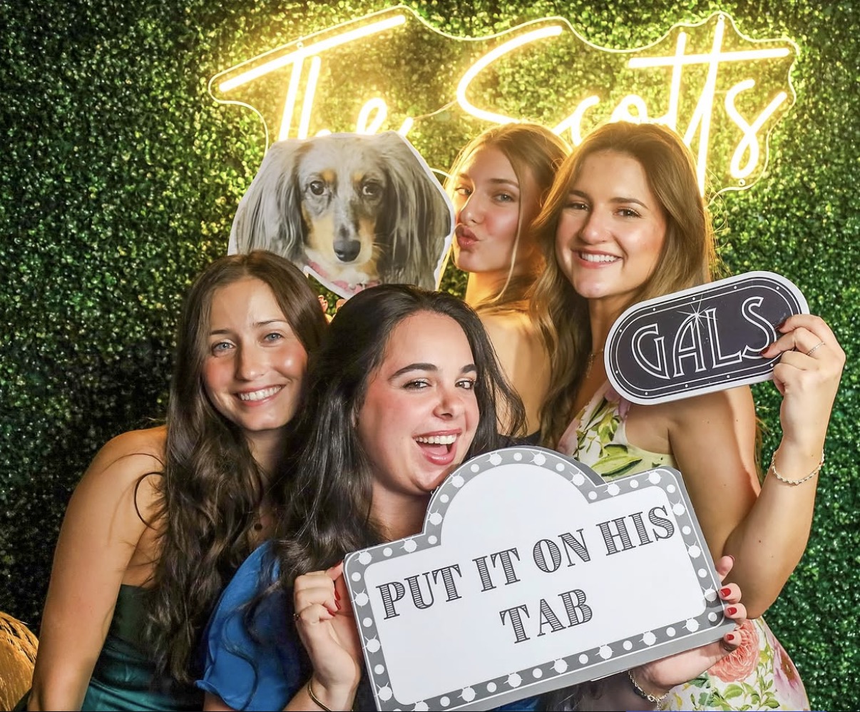 Wedding guests with fun props at greenery wall photo booth