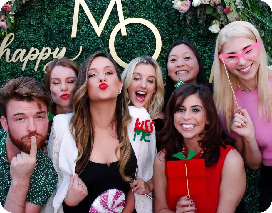 Friends posing with props at photo booth with greenery and floral backdrop